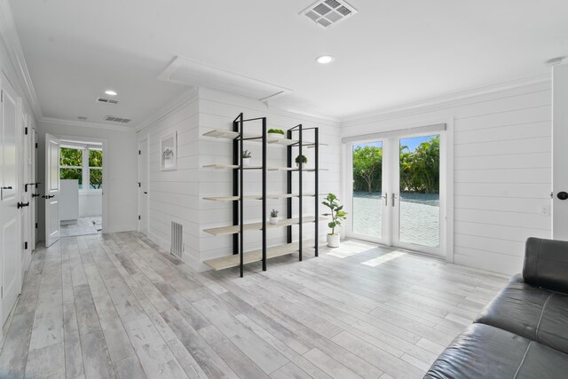 unfurnished living room featuring ornamental molding, light wood-type flooring, and french doors