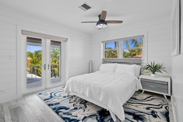 bedroom with french doors, wood walls, access to outside, hardwood / wood-style flooring, and ceiling fan