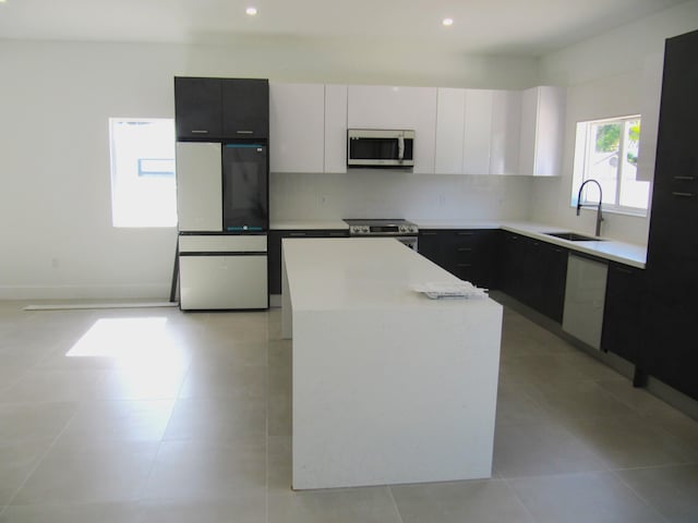 kitchen featuring appliances with stainless steel finishes, white cabinetry, sink, backsplash, and a center island