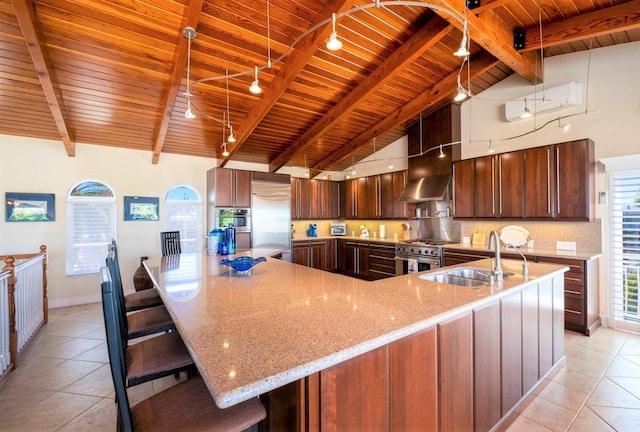 kitchen with light tile patterned flooring, high quality appliances, sink, a kitchen breakfast bar, and beam ceiling