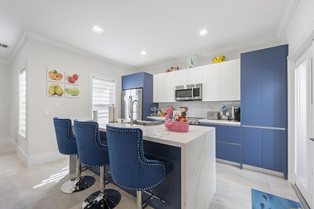 kitchen featuring stainless steel appliances, ornamental molding, a kitchen island with sink, and a kitchen bar