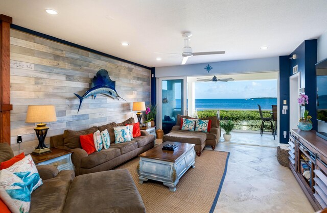 living room with wooden walls, ceiling fan, and a water view