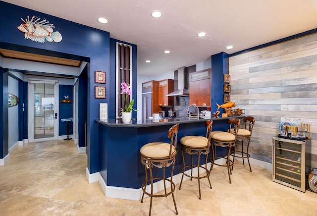 bar with wall chimney range hood, wooden walls, and beverage cooler