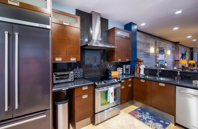 kitchen featuring appliances with stainless steel finishes, sink, dark stone countertops, decorative backsplash, and wall chimney exhaust hood