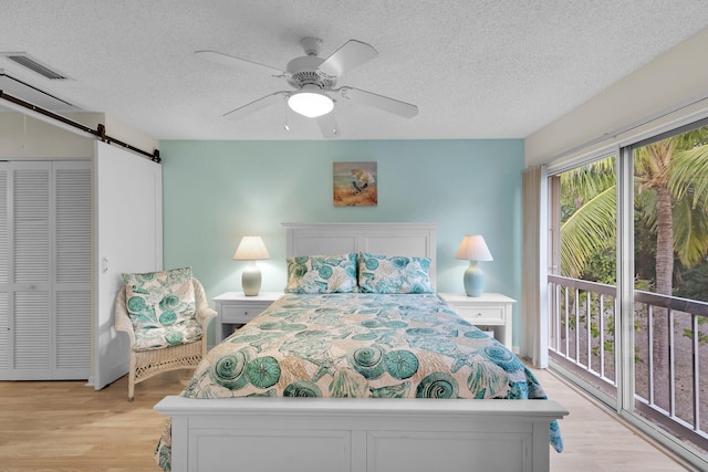 bedroom featuring ceiling fan, access to exterior, light hardwood / wood-style floors, a textured ceiling, and a barn door