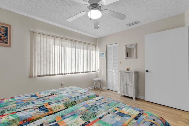 bedroom featuring ceiling fan, a textured ceiling, light hardwood / wood-style floors, and a closet