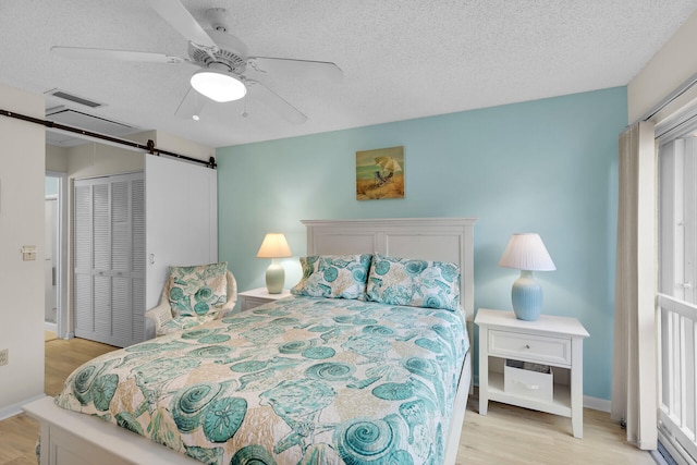 bedroom with ceiling fan, a barn door, a textured ceiling, and light wood-type flooring