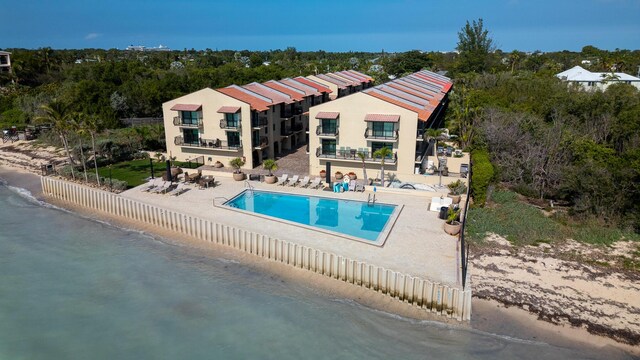 back of property with a view of the beach, a water view, a balcony, a community pool, and a patio