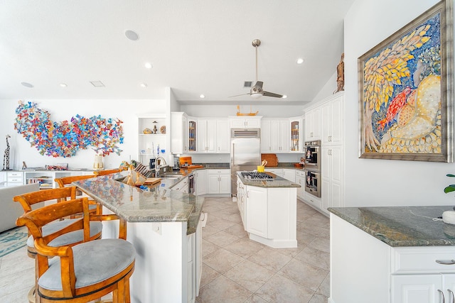 kitchen featuring stainless steel appliances, a center island, white cabinets, and dark stone counters