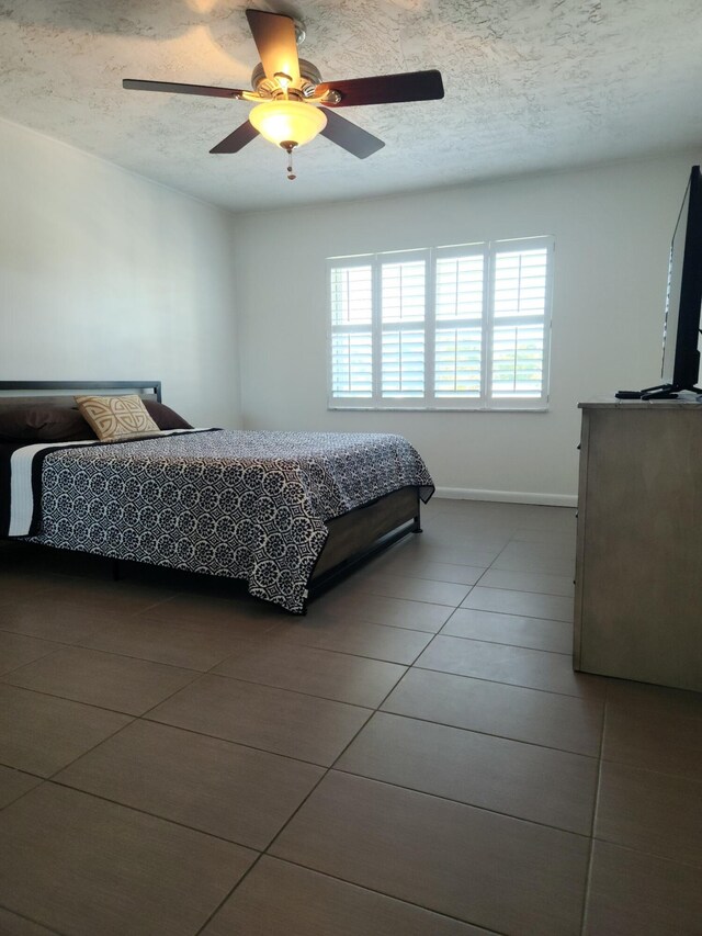 tiled bedroom with ceiling fan and a textured ceiling