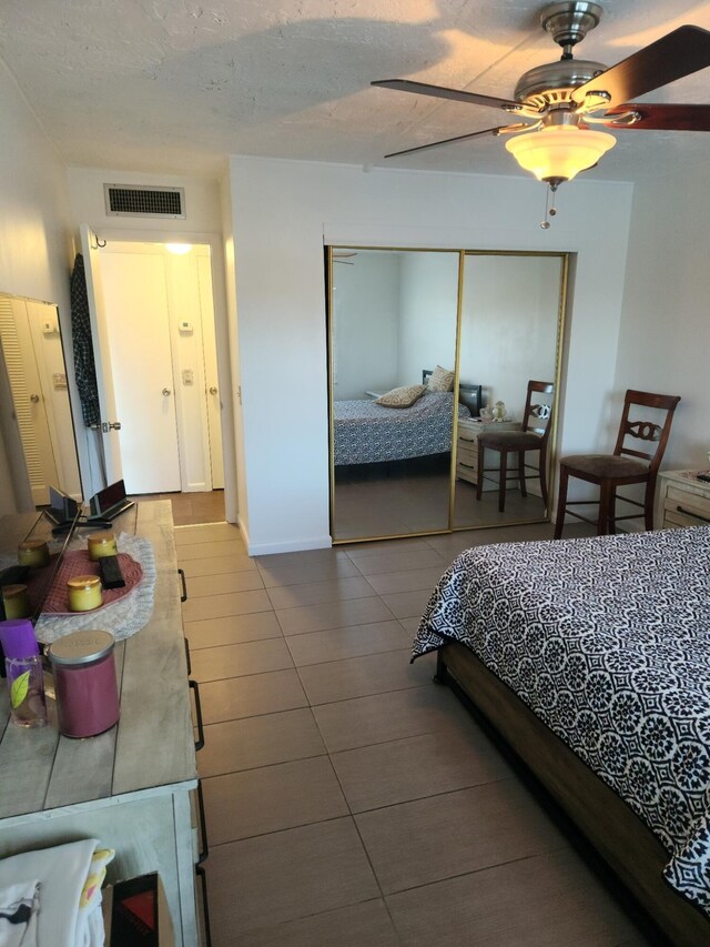 bedroom with a textured ceiling, tile patterned floors, visible vents, a ceiling fan, and a closet