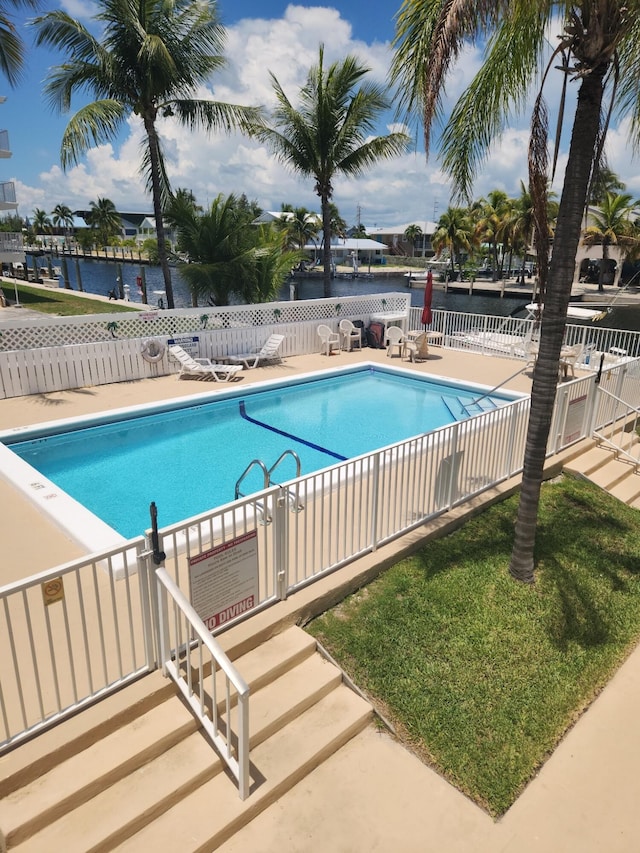 community pool with a patio area, a water view, and fence
