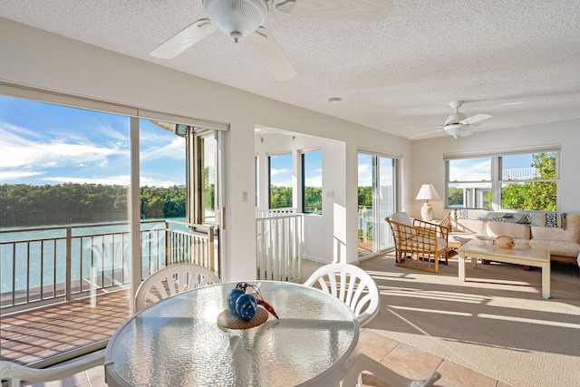 sunroom / solarium with plenty of natural light, ceiling fan, and a water view