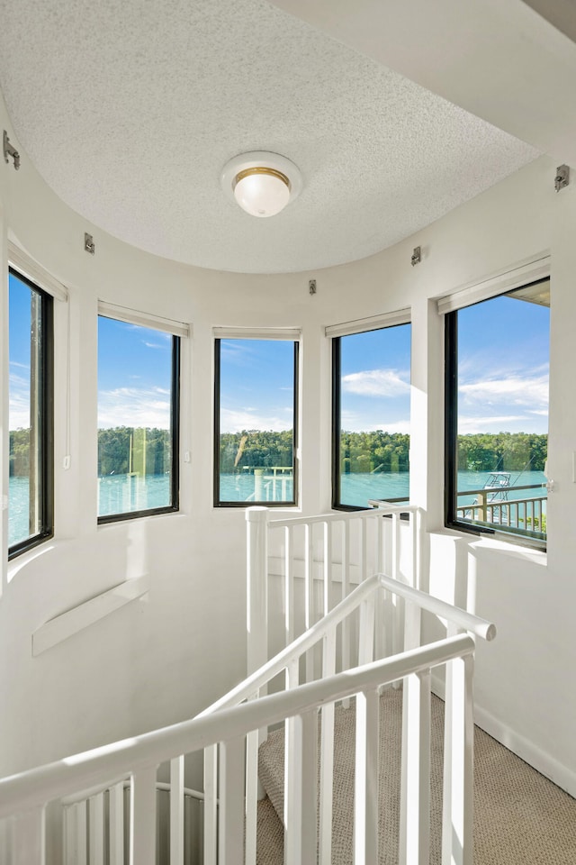 interior space featuring a water view, carpet flooring, and a textured ceiling