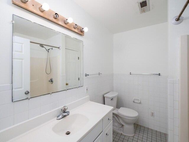 bathroom with tile walls, tile patterned flooring, vanity, walk in shower, and toilet