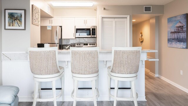 kitchen featuring white cabinetry, appliances with stainless steel finishes, a kitchen breakfast bar, and decorative backsplash