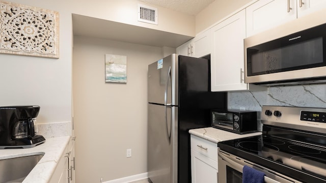 kitchen featuring white cabinetry, appliances with stainless steel finishes, light stone countertops, and backsplash