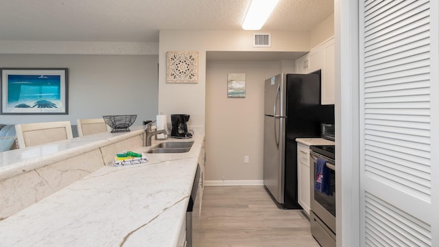 kitchen with sink, a breakfast bar area, white cabinetry, appliances with stainless steel finishes, and light stone countertops