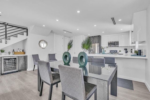 dining space featuring bar area, beverage cooler, and light wood-type flooring