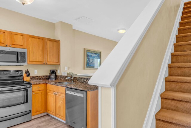 kitchen featuring stainless steel appliances, sink, dark stone countertops, and light hardwood / wood-style floors