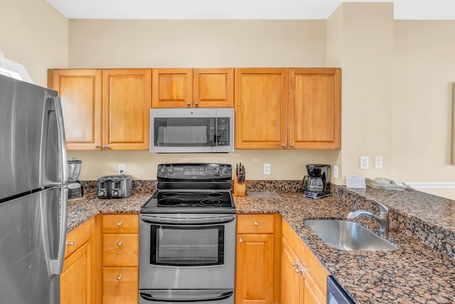 kitchen featuring stainless steel appliances, sink, and dark stone countertops