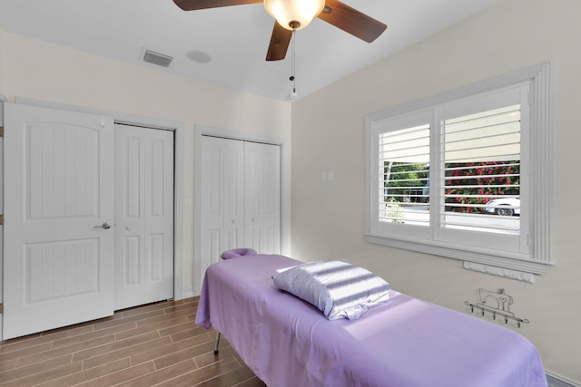 bedroom with visible vents, wood finish floors, a ceiling fan, and multiple closets