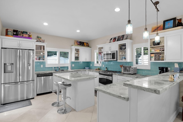 kitchen with white cabinetry, open shelves, a peninsula, appliances with stainless steel finishes, and a kitchen bar