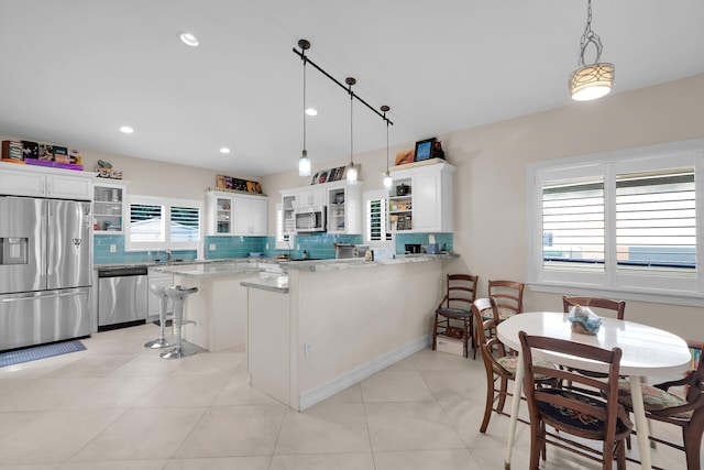 kitchen with a peninsula, stainless steel appliances, decorative backsplash, glass insert cabinets, and white cabinetry