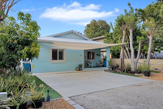 back of house with gravel driveway, metal roof, and stucco siding