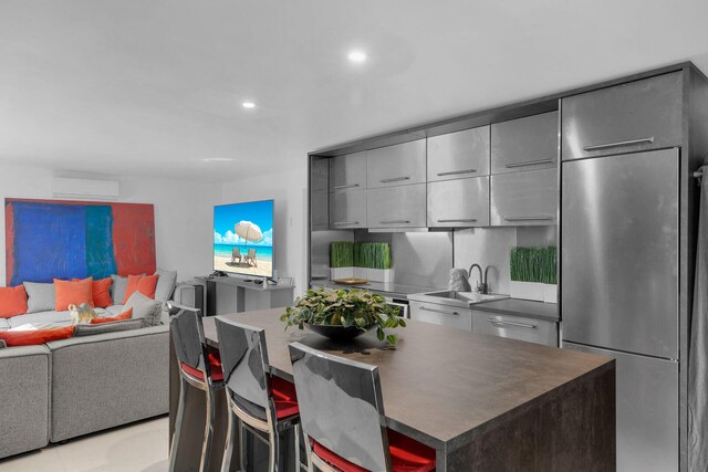 kitchen with sink, gray cabinets, stainless steel refrigerator, a kitchen breakfast bar, and a kitchen island