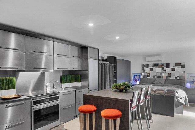 kitchen featuring gray cabinets, a kitchen island, a kitchen bar, stainless steel oven, and black electric cooktop