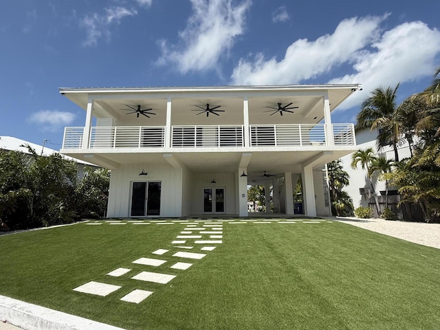 back of house with board and batten siding, a lawn, french doors, a balcony, and a ceiling fan