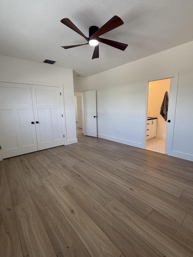 unfurnished bedroom featuring wood finished floors, baseboards, visible vents, a closet, and a textured ceiling