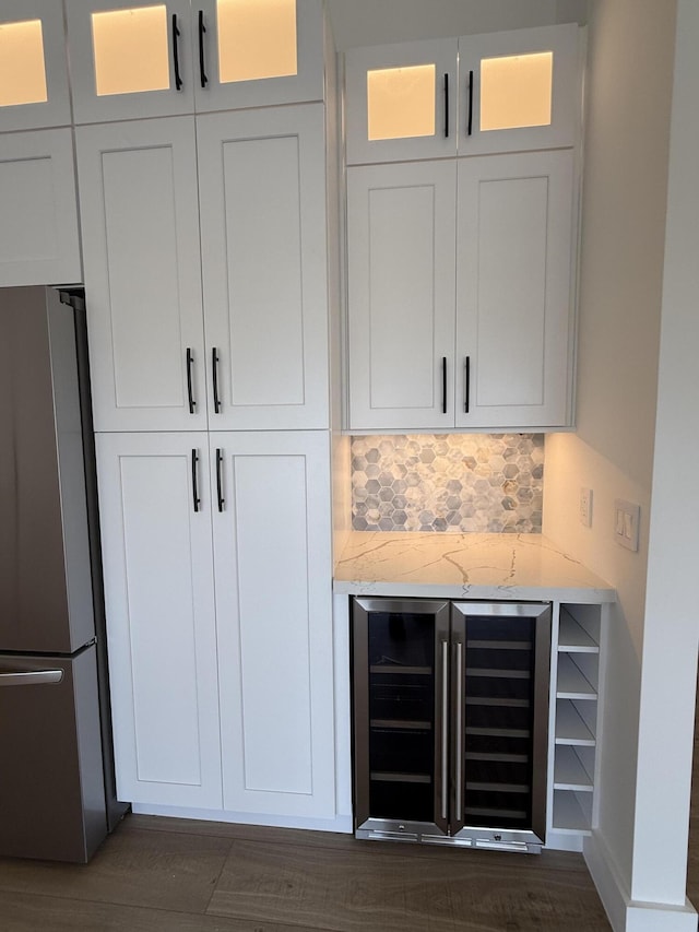 room details featuring glass insert cabinets, wine cooler, light stone counters, freestanding refrigerator, and a bar