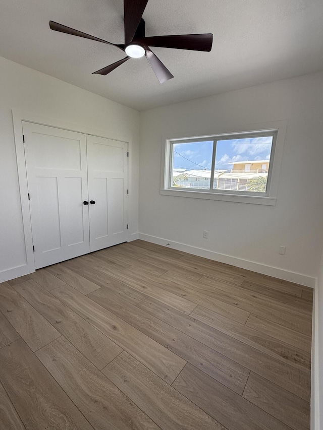 unfurnished bedroom featuring a closet, a ceiling fan, light wood-type flooring, and baseboards