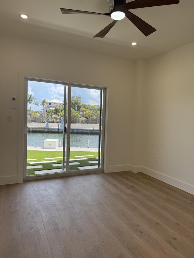 empty room featuring wood finished floors, recessed lighting, a ceiling fan, and a water view