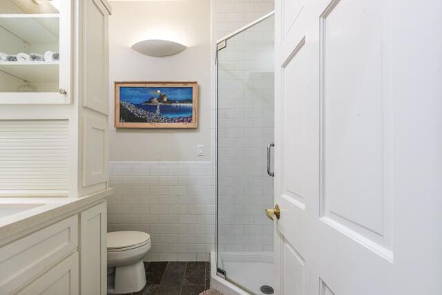 full bathroom featuring a stall shower, toilet, tile walls, vanity, and a wainscoted wall