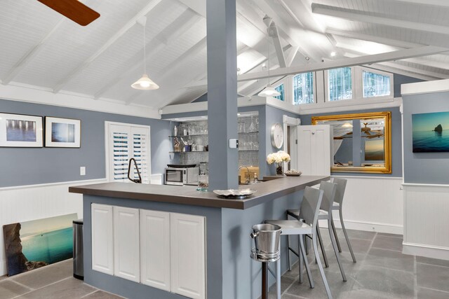 kitchen featuring white cabinetry, a breakfast bar, pendant lighting, and vaulted ceiling with beams