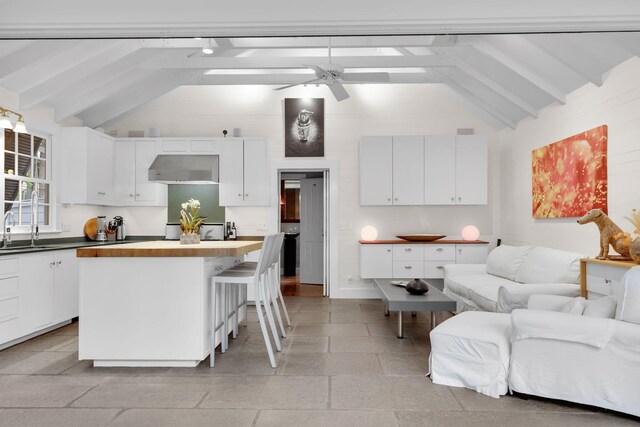 kitchen featuring sink, ceiling fan, white cabinetry, a kitchen island, and beamed ceiling