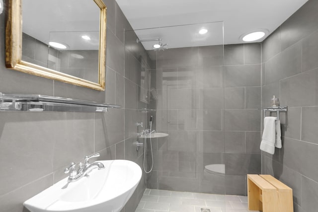 bathroom with sink, a tile shower, and tile walls