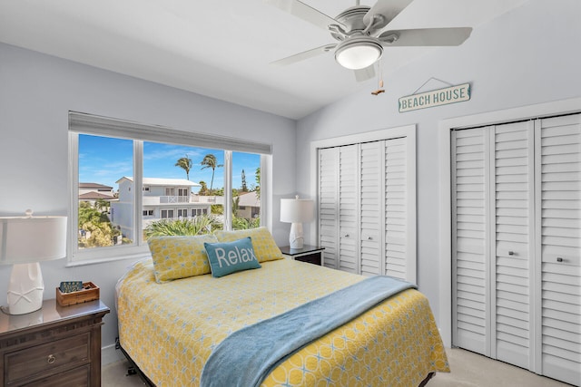 bedroom featuring lofted ceiling, carpet flooring, two closets, and ceiling fan