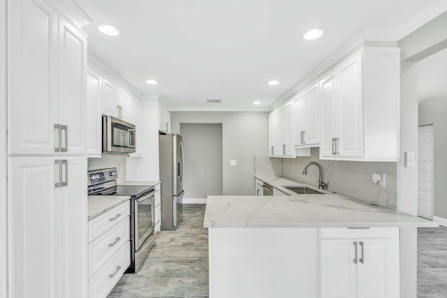 kitchen featuring a peninsula, a sink, white cabinetry, appliances with stainless steel finishes, and light stone countertops