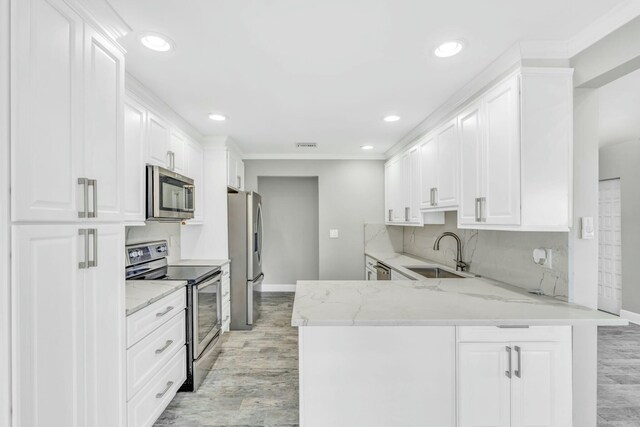 kitchen featuring a peninsula, light stone countertops, stainless steel appliances, white cabinetry, and a sink