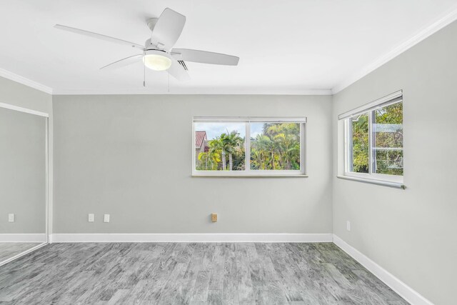 empty room with ornamental molding, wood finished floors, a ceiling fan, and baseboards