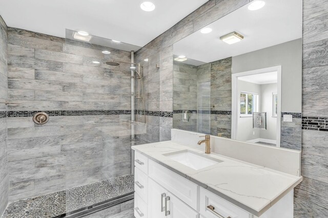 full bathroom with tiled shower, tile walls, and vanity