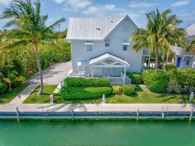 back of house with metal roof, a water view, and a lawn