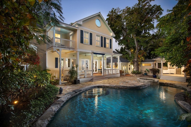 back house at dusk with french doors, ceiling fan, a balcony, and a patio area