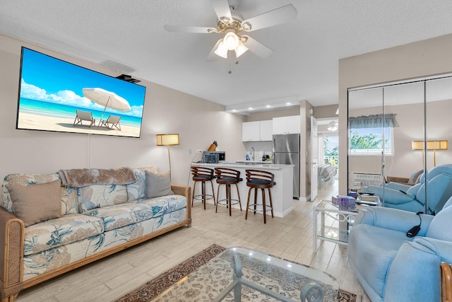 living room featuring ceiling fan, a textured ceiling, and light wood-type flooring