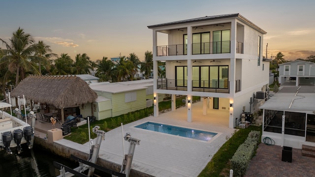 rear view of house with an outdoor pool, a ceiling fan, a balcony, boat lift, and a patio area