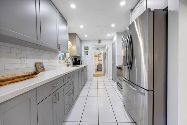 kitchen with sink, light tile patterned floors, gray cabinets, stainless steel appliances, and decorative backsplash